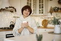 Happy beautiful middle aged woman enjoying drinking tea or coffee in kitchen with Christmas decor Royalty Free Stock Photo