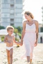 Happy beautiful mom goes hand in hand with smiling child at the sand beach