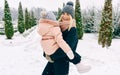 Happy beautiful mother holding her child in arms, smiling broadly during walking in the park on snowing day. Young woman and her Royalty Free Stock Photo