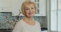 Happy beautiful older middle aged woman look at camera on the kitchen background. Elderly, beautiful woman smiling