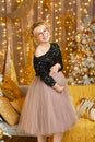 Happy beautiful pregnant woman in a blue blouse and pink skirt standing near new year tree and laughs in a yellow studio Royalty Free Stock Photo