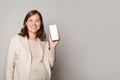 Happy beautiful pregnant woman showing her mobile phone with white empty display and smiling against grey studio wall background Royalty Free Stock Photo