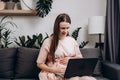 Happy beautiful pregnant woman sitting on cozy sofa using laptop having video call conversation to family, talk to obstetrician- Royalty Free Stock Photo