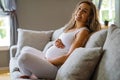 Happy beautiful pregnant woman sitting in sofa touching her belly Royalty Free Stock Photo