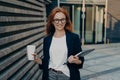 Happy beautiful red-haired businesswoman with laptop and paper cup of coffee in hands outdoors Royalty Free Stock Photo