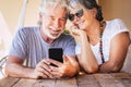 Happy beautiful senior old couple do a phone call with modern online technology device - retired cheeful people together forever