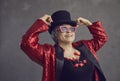 Happy beautiful senior woman in top hat, stylish glasses and bling jacket posing in studio