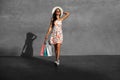 Happy beautiful shopaholic woman carrying shopping bags in city against urban gray wall background Royalty Free Stock Photo