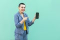 Happy beautiful with short hair young woman in striped suit standing, holding phone and pointing finger to it, toothy smile and Royalty Free Stock Photo