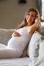 Happy beautiful pregnant woman sitting in sofa touching her belly Royalty Free Stock Photo