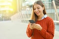 Happy beautiful student woman writing or reading sms messages online on a smart phone while standing in modern city street. Copy Royalty Free Stock Photo