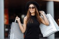 Happy beautiful stylish Shopaholic girl, in a black dress, black hat and sunglasses, stands with shopping bags in the city against Royalty Free Stock Photo