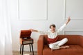 Happy beautiful teenager boy sitting on brown sofa with hands rising and eyes closed, listening vinyl record on retro wooden Royalty Free Stock Photo