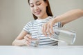 Happy beautiful, thirsty asian young woman, girl drinking, hand in holding, pouring water from jug into transparent glass from Royalty Free Stock Photo