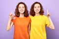 Happy beautiful twins girls point up isolated on blue background