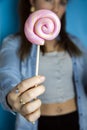 Happy beautiful woman giving colorful pink twirl lollipop on light blue background. Sweets,hard candy,gift,