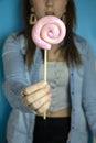 Happy beautiful woman giving colorful pink twirl lollipop on light blue background. Sweets,hard candy,gift