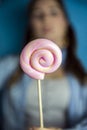 Happy beautiful woman giving colorful pink twirl lollipop on light blue background. Sweets,hard candy,gift