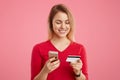 Happy beautiful woman holds smart phone and credit card, makes online payment, pays for purchase in online shop or verifies her ba Royalty Free Stock Photo