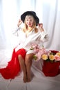 Happy beautiful woman with long blond hair and in black hat posing with flowers in studio on white background Royalty Free Stock Photo