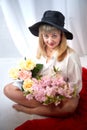 Happy beautiful woman with long blond hair and in black hat posing with flowers in studio on white background Royalty Free Stock Photo