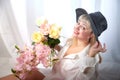 Happy beautiful woman with long blond hair and in black hat posing with flowers in studio on white background Royalty Free Stock Photo