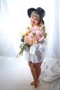 Happy beautiful woman with long blond hair and in black hat posing with flowers in studio on white background Royalty Free Stock Photo