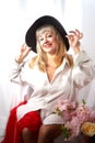 Happy beautiful woman with long blond hair and in black hat posing with flowers in studio on white background Royalty Free Stock Photo