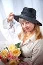 Happy beautiful woman with long blond hair and in black hat posing with flowers in studio on white background Royalty Free Stock Photo