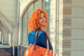 Happy beautiful woman looking over shoulder, holding orange leather bag, isolated street background. Pretty young girl with red Royalty Free Stock Photo