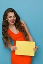 Happy Beautiful Woman In Orange Dress Is Holding Yellow Sheet Of Paper And Laughing Royalty Free Stock Photo