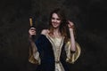 Happy beautiful woman in renaissance dress styling her hair with a curling iron on abstract dark background Royalty Free Stock Photo