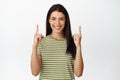 Happy beautiful woman smiling, pointing fingers up, showing advertisement, standing in t-shirt over white background Royalty Free Stock Photo