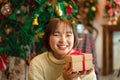 Happy beautiful woman in sweater is smiling and holding present box in front of the christmas tree and decoration Royalty Free Stock Photo