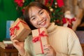 Happy beautiful woman in sweater is smiling and holding present box in front of the christmas tree and decoration Royalty Free Stock Photo