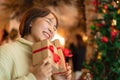 Happy beautiful woman in sweater is smiling and holding present box in front of the christmas tree and decoration Royalty Free Stock Photo