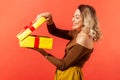 Happy beautiful woman unboxing big yellow present and looking inside with satisfied smile on face, enjoying present Royalty Free Stock Photo