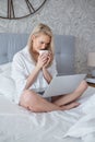 Happy beautiful woman working on a laptop sitting on the bed in the house. Royalty Free Stock Photo