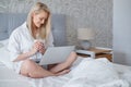 Happy beautiful woman working on a laptop sitting on the bed in the house. Royalty Free Stock Photo