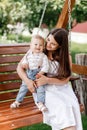 Happy beautiful woman, young mother playing with her adorable baby son and sitting on wooden swing, cute little boy Royalty Free Stock Photo