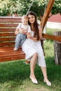 Happy beautiful woman, young mother playing with her adorable baby son and sitting on wooden swing, cute little boy Royalty Free Stock Photo