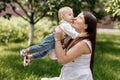 Happy beautiful woman, young mother playing and kissing her adorable baby son, cute little boy, enjoying together a sunny warm day Royalty Free Stock Photo