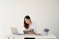 Happy Asian businesswoman is taking notes on her personal notebook, looking at her laptop screen Royalty Free Stock Photo