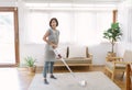 Happy beautiful young Asian woman doing house chores in apron using vacuum cleaning the carpetin a cozy room at home. Cleaning day Royalty Free Stock Photo