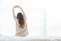 Happy beautiful young Asian woman waking up in morning, sitting on bed, stretching in cozy bedroom, looking through window. Royalty Free Stock Photo