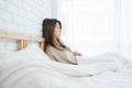 Happy beautiful young Asian woman waking up in morning, sitting on bed, stretching in cozy bedroom, looking through window. Royalty Free Stock Photo