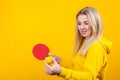 Happy beautiful young blonde woman in casual yellow sporty clothes play ping pong, holding a ball and racquet Royalty Free Stock Photo