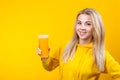 Happy beautiful young blonde woman in yellow casual sporty clothes holding orange juice glass Royalty Free Stock Photo