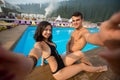 Happy beautiful young couple sitting at the edge of the swimming pool and taking selfie photo Royalty Free Stock Photo