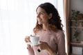 Happy beautiful young dreamy woman standing near window with cup of tea. Royalty Free Stock Photo
